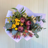 Bouquet of flowers with proteas and yellow strawflowers on a light wooden background