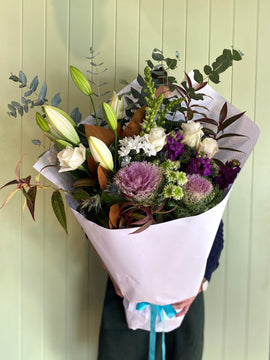Bouquet of flowers with a white paper wrap held by a person against a light green wooden panel background