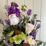 White pot of flowers with purple, white, and green colors on a light background