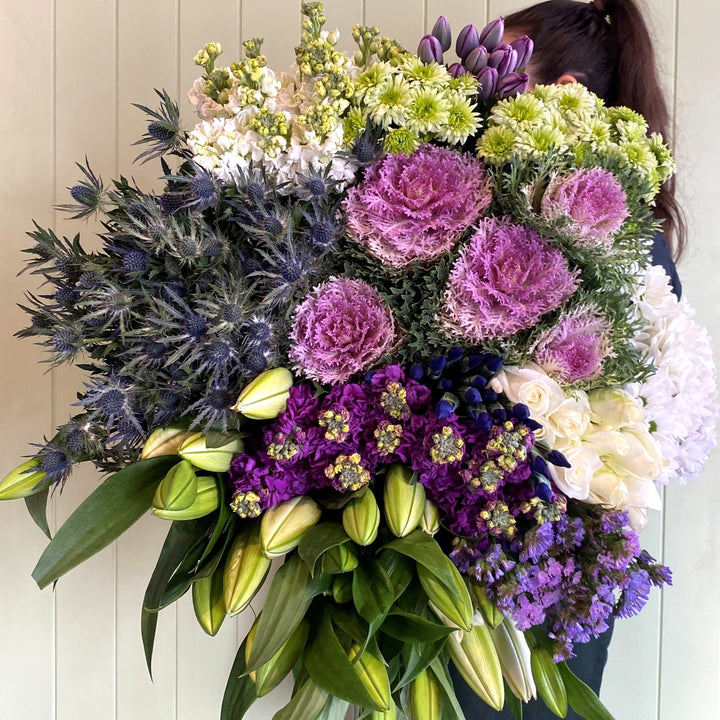 Person holding a huge bundle of colorful flowers including purple, green, and white flowers.