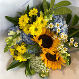 Bouquet of flowers with sunflowers, yellow and blue flowers, and green leaves on a white background.