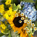 Bouquet of flowers with sunflowers, hydrangeas, and other greenery on a white surface.