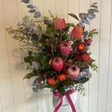 Bouquet of flowers with pink and red tones in a clear vase against a white wooden panel background