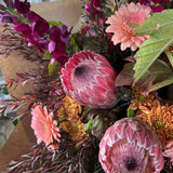 Bouquet of flowers with protea, pink and orange flowers, and green leaves.