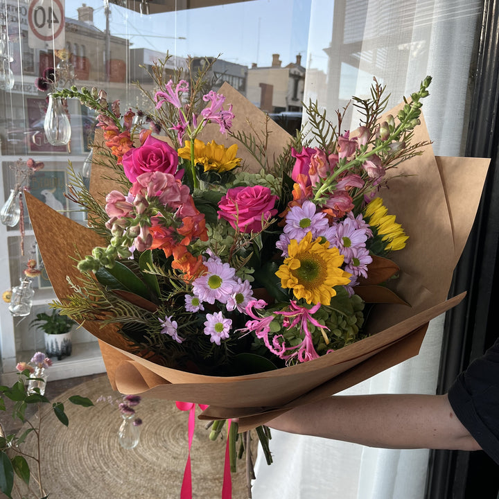 Bouquet of bright, colourful flowers wrapped in brown paper.