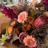 Bouquet of native flowers in tones of peach, rust and burgundy with brown paper wrap
