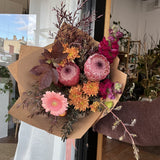 Bouquet of native flowers in pink, peach, rust and burgundy wrapped in brown paper 