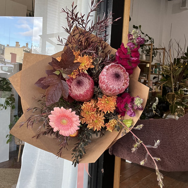 Bouquet of native flowers in pink, peach, rust and burgundy wrapped in brown paper 