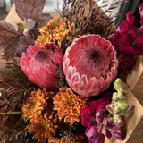 Bouquet of pink protea flowers and orange chrysanthemums wrapped in brown paper.
