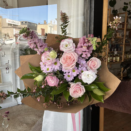 Bouquet of soft pink and lilac flowers in a brown paper wrap.
