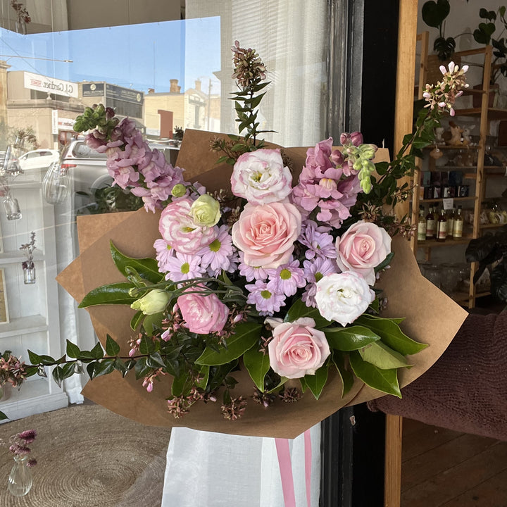 Bouquet of soft pink and lilac flowers in a brown paper wrap.