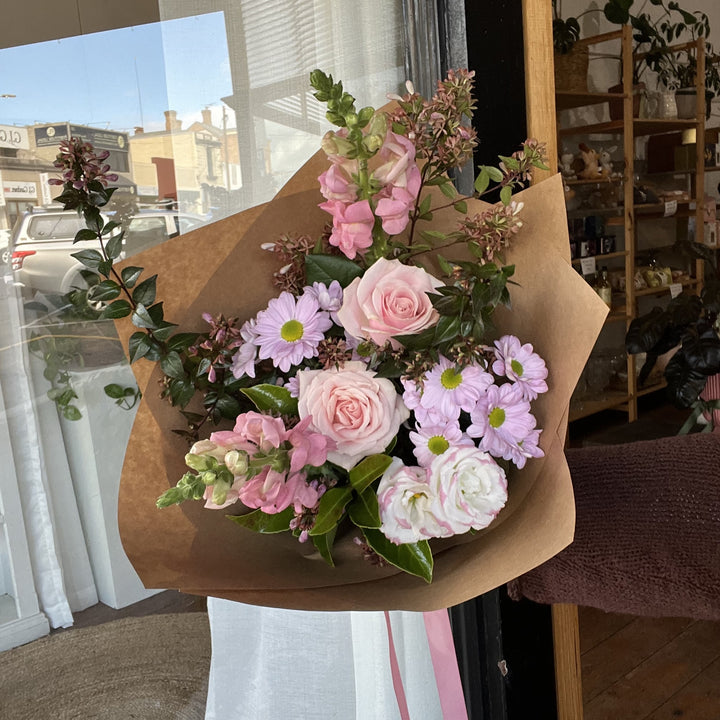 Bouquet of soft pink, pale purple and white flowers wrapped in brown paper