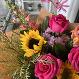 Bright bouquet of flowers including sunflowers and roses in brown paper.
