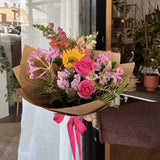 Bright bouquet of flowers with a hot pink ribbon. Featuring a sunflower and hot pink roses.