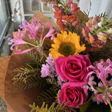 Bright bouquet of flowers including hot pink roses and sunflowers in brown paper.