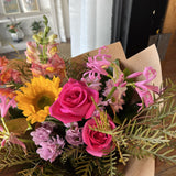 Bouquet of flowers with pink roses, sunflowers, and other varieties in a brown paper.