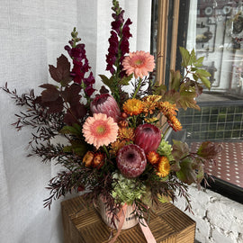 A flower arrangement in a vase with earthy, native flowers in pink, peach, rust and burgundy