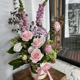 Arrangement of soft pink mauve and white flowers in a vase with a pink ribbon