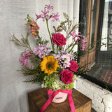 Bright, vibrant flower arrangement in a pot with hot pink roses and a sunflower