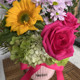 Arrangement of flowers with a hot pink rose, yellow sunflower, and green hydrangea, in a vase with a hot pink ribbon
