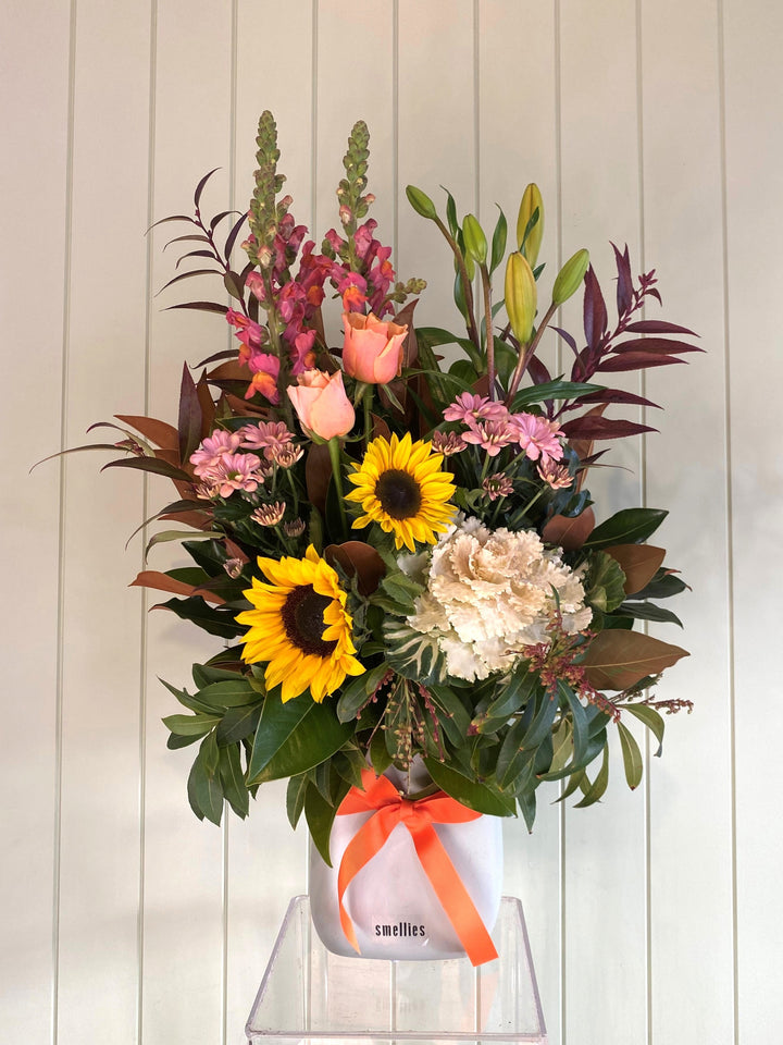 Bouquet of flowers with sunflowers and pink roses in a white box on a light wooden background