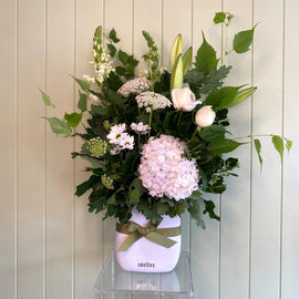 A ceramic vase floral arrangement featuring white and pink flowers with green foliage, presented on a wooden surface.