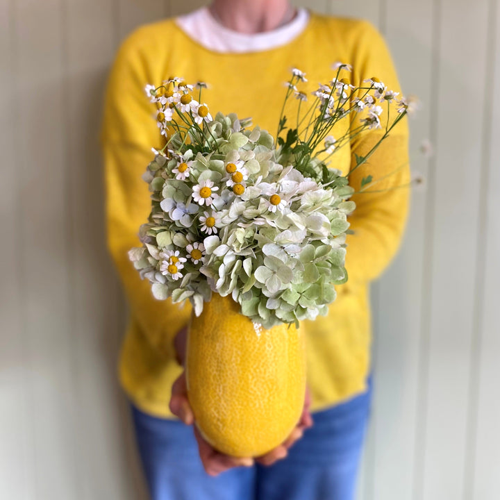 Person holding a yellow vase with flowers against a neutral background
