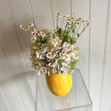 Yellow vase with flowers on a white wooden shelf