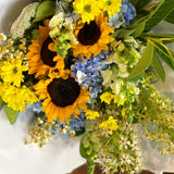 Bouquet of sunflowers, blue flowers, and greenery on a white background