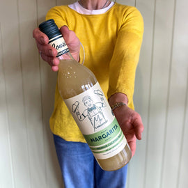 Person holding a bottle of 'Margarita' with a label featuring a cartoon character against a white paneled wall.