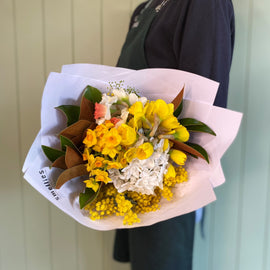 Person holding a posie of fragrant yellow and white jonquils and daffodils against a wall