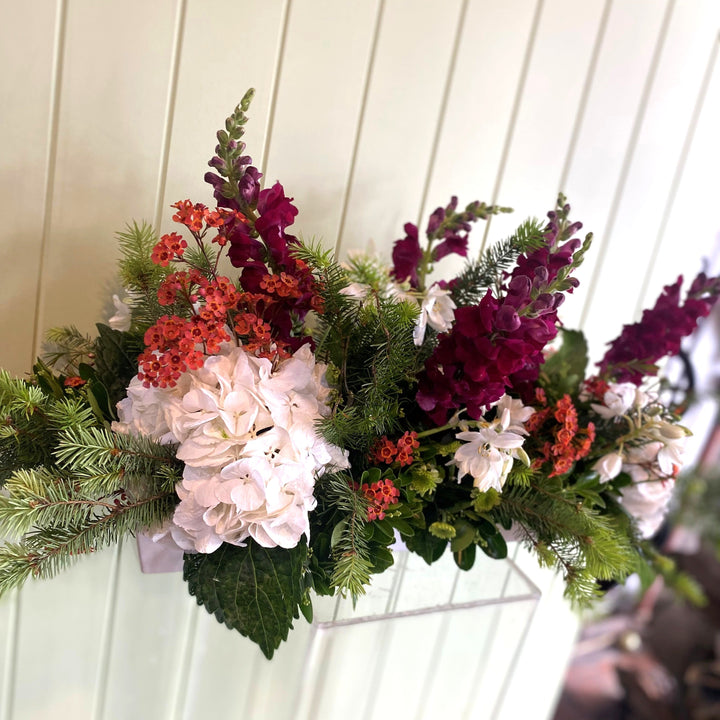 Christmas floral arrangement in a white ceramic pot with against a white wooden panel background