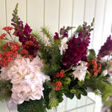 Arrangement of flowers with red, burgundy, and white flowers against a white wooden panel background