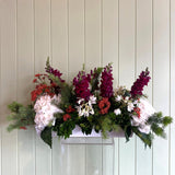 Floral arrangement in a white pot against a light wooden panel background