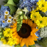 Bouquet of flowers with sunflowers, blue and yellow hydrangeas, and greenery on a white background.
