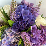 Bouquet of purple and white flowers with green leaves on a light background