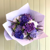 Bouquet of purple and white flowers wrapped in paper on a wooden surface