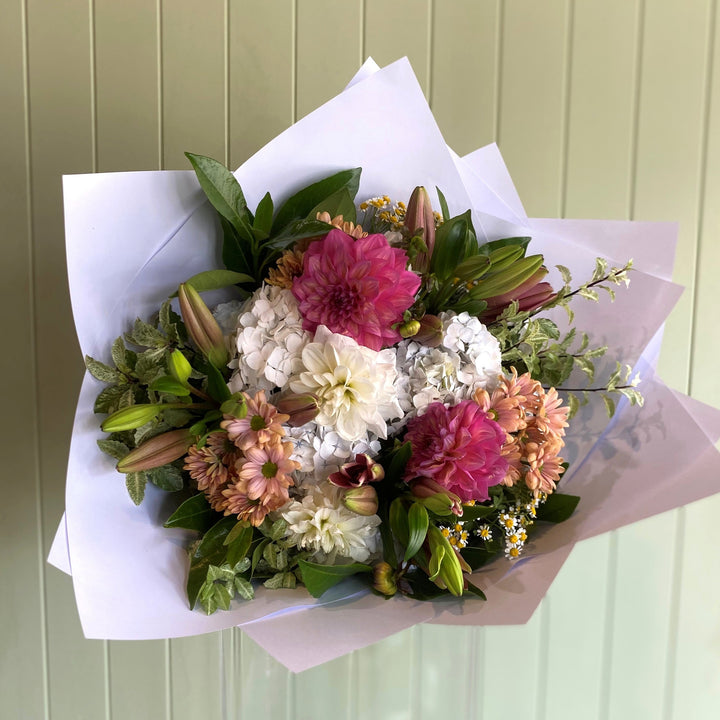 Bouquet of flowers wrapped in paper against a light green wooden panel background