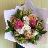 Bouquet of flowers wrapped in white paper against a light green wall.