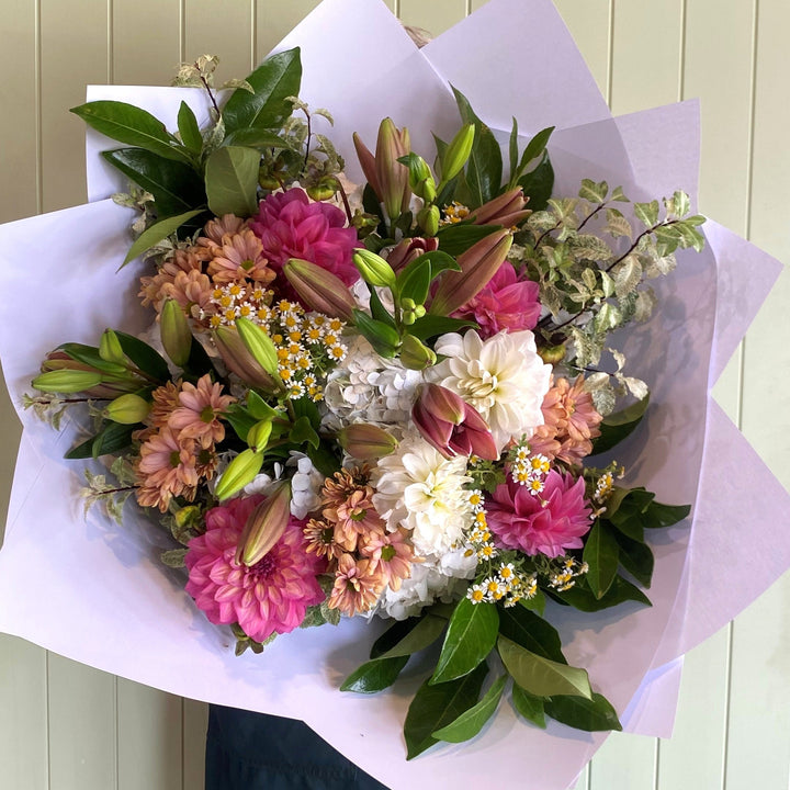 Bouquet of flowers wrapped in paper against a light green wall.