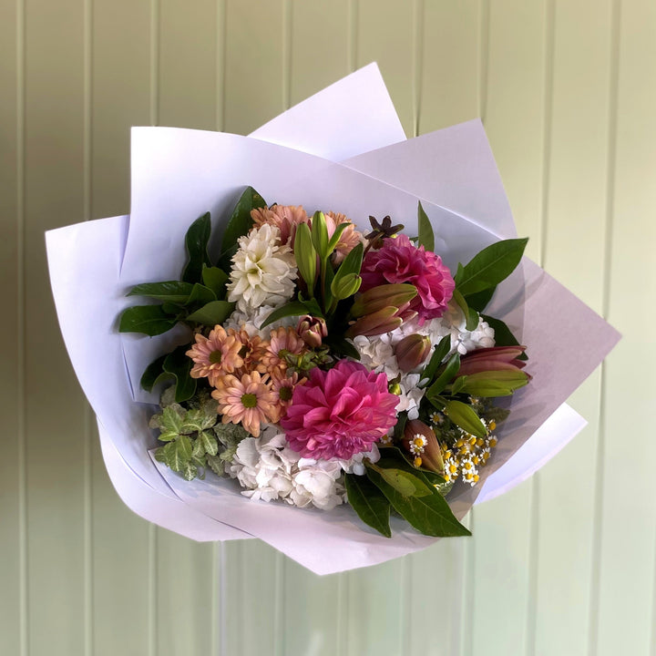 Bouquet of flowers wrapped in white paper against a light green wall.