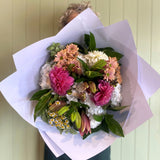 Person holding a bouquet of flowers wrapped in white paper against a light green wall.