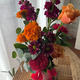 Arrangement of bright, colourful flowers in a vase with a pink ribbon.
