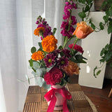 Arrangement of bright, colourful flowers in a vase with a pink ribbon.