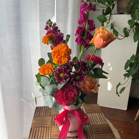 Arrangement of bright, colourful flowers in a vase with a pink ribbon.