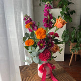 Arrangement of bright, colourful flowers in a vase with a pink ribbon.