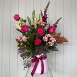 Bouquet of flowers with pink and purple tones in a clear vase against a white background