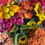 The COCKTAIL POSIE OF THE DAY by Smellies Flowers showcases premium sunflowers, pink and peach roses, orange ranunculus, yellow button flowers, and chrysanthemums with lush greenery for a vibrant, sustainable touch.