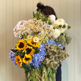 Person holding a large bouquet of flowers in a room with shelves and a door.