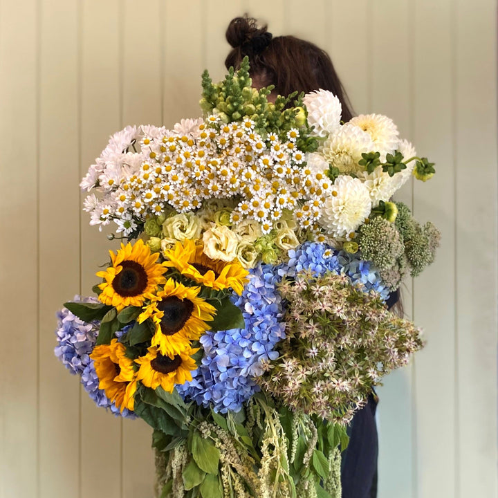 Person holding a large bouquet of flowers in a room with shelves and a door.